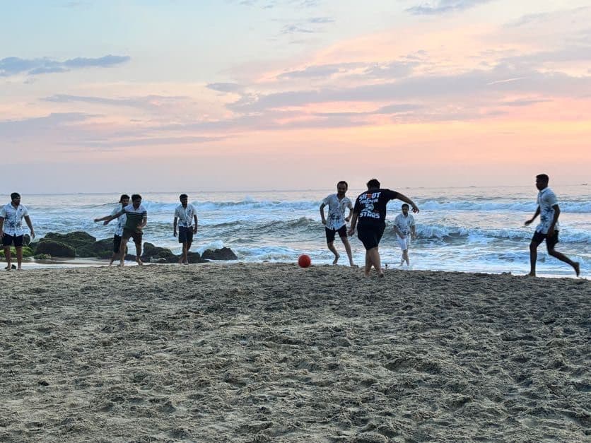 The INTEGRTR team playing football on a Kerala beach at dusk, surf breaking behind them.